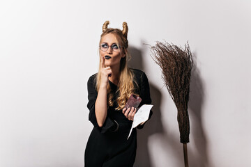 Charming witch in glasses posing on white background. Indoor photo of pensive vampire girl enjoying halloween party.