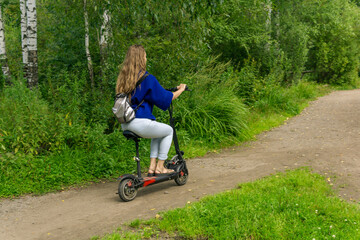 young woman rides an electric scooter along the path in the park