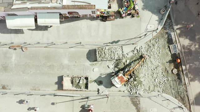Drone shot from top view on a small excavator digging stone paving stones in the old town of Gdansk, Poland. Repair of paving stones on the street of the old town.