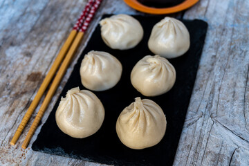Dim Sum, traditional Japanese food, served on a black slate plate, with a bowl of soy sauce and some chopsticks, on a rustic wooden background.