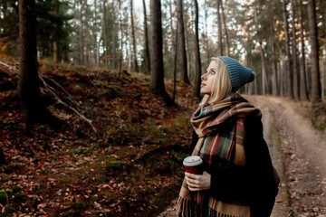 Beautiful blond girl in blue hat with cup of coffee in a forest