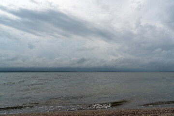 Seashore with sand and shells at sunrise. Cloudy sky and fog on the horizon.