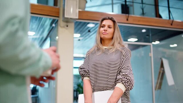 Zoom in of two business people in casual, man with coffee and woman with laptop, talking at break in office hall. Female entrepreneur listening to male colleague explaining ideas and nodding head