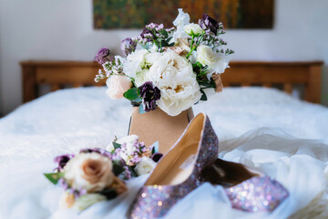 Bridal bouquet with fresh eucalyptus, peony and eustoma flowers posy with wedding shoes and floral hair decor on the bed in fine art style. Selective focus, copy space.