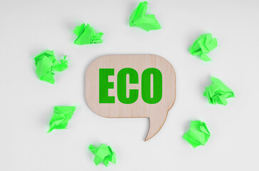 On a white background, there are crumpled green pieces of paper and a wooden sign with the inscription - ECO