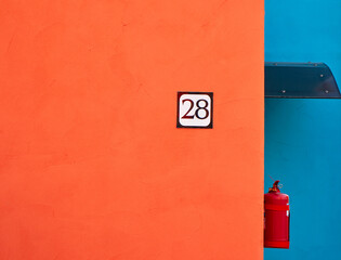 plate with the numbers 28 on an orange with a blue wall next to a fire extinguisher