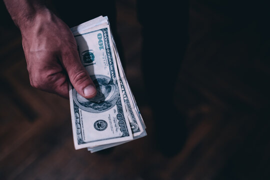 Closeup shot of a male hand holding US dollars over a wooden parquette