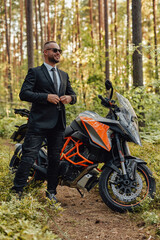 Fototapeta na wymiar Joyful man in costume with dark motorcycle in woods