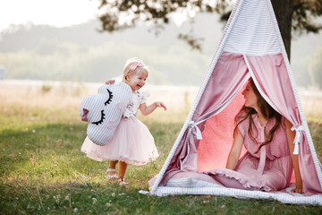 Beautiful mother with her little daughter sitting near wigwam in the park. Spending time together, outside, on vacation, outdoors © Andriy Medvediuk