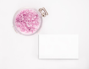 Jar with soft pink granules of sea salt in a transparent glass jar with a place for a business card