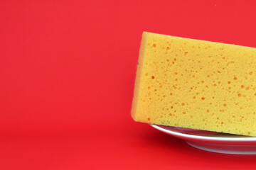 yellow sponge for washing dishes on a plate on a red background, a place for text.