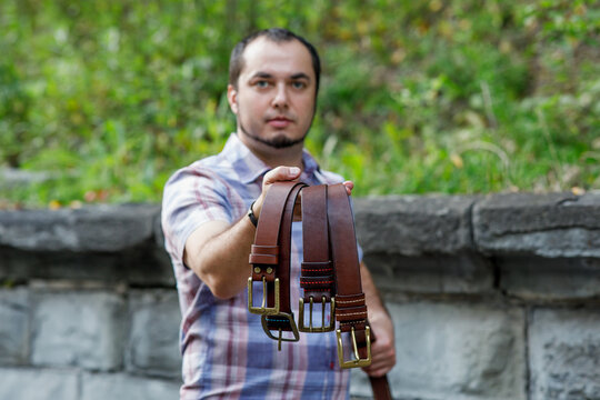 Master saddler holds genuine leather belts for men. Accessories with brass buckle.