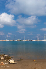 view from a rocky wild beach to white yachts moored at the pier in the Greek town of Rethymnon against a background of blue sky