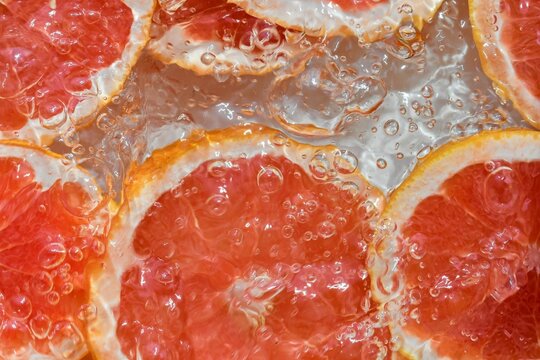 Grapefruit Close-up In Liquid With Bubbles. Slice Of Blood Red Ripe Grapefruit In Water. Close-up Fresh Slices Of Red Grapefruit On White Background