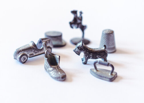 Original Monopoly player markers are scattered on a white background.  Selective focus.  Markers included: shoe, iron, dog, car, thimble, hat, and horse.