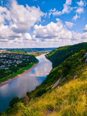 Fototapeta na wymiar Large river flows in a green valley with wooded hills. Town on the river. Beautiful landscape with bright sun and nature. 