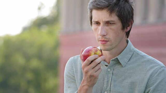 Modern products odorless and tasteless. Millennial guy wants to have breakfast with fruit discovers that ripe, juicy fresh apple from new crop does unscented. Worried man tests his sense of smell