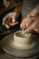 a child and an adult rotate the clay on a potter's wheel
