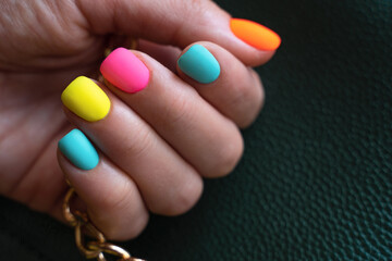 The palm with bright colored nails with orange, pink, blue, yellow colors hold green bag. Rainbow colors 