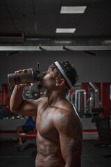 Fototapeta na wymiar Sportive african american man with naked torso drink water or sports nutrition after training in gym