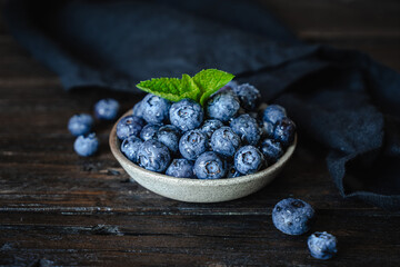 Ripe juicy blueberries with mint leaves and drops of water in a ceramic bowl on an old wooden table. Healthy food, vegetarian concept, rustic style, top view. Freshly picked blueberries. © Ksenya