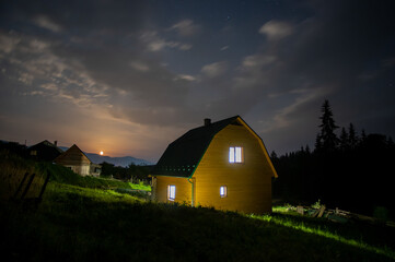 Night landscape, wooden house in a village near the forest in the mountains in summer