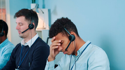 Medium shot of Bored and dissatisfied black call center agent talking to the client on phone. He is...