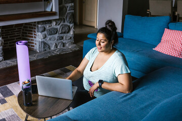 Young mexican plus size woman using laptop sitting on the floor in the living room in Latin America