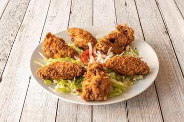 Fried wings with crispy batter on a bed of lettuce, tomato and raw onion on a white plate
