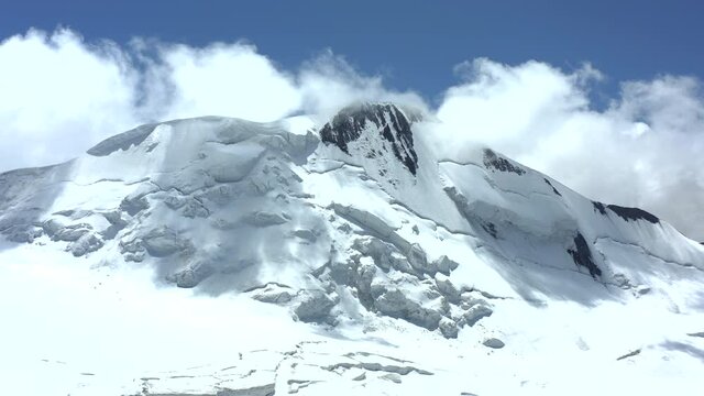 Aerial view of flying a drone straight ahead. Mountain covered with snow blue sky and clouds. A huge glacier and an impregnable mountain covered with eternal snow