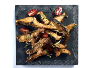 strips of fried fish with tomato served on stone on white background.