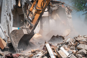 Hydraulic excavator bucket breaks down old building. Wreckage and industrial debris in dust, house...