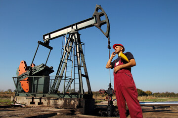 Petroleum engineer with red hard hat and red work overalls, holding data folder, using smartphone in an oilfield