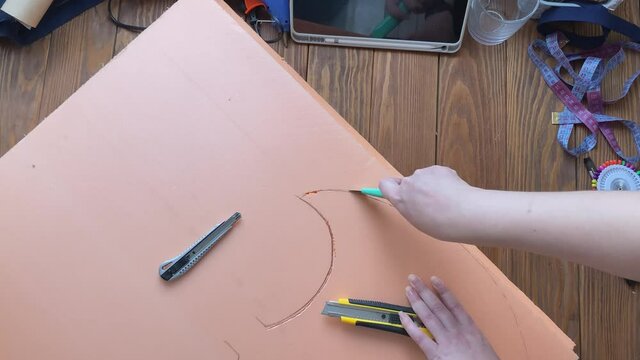 Woman makes viking axe for cosplay festival. Hands cut hatchet form from foam polystyrene with stationary knife. Craftsman's workshop. Diy celtic weapon on wooden table.
