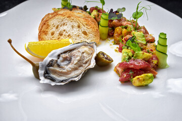 Oyster on a white plate with lemon, crouton and tartare