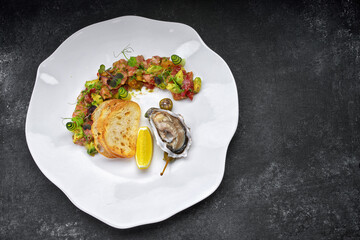 Oyster on a white plate with lemon, crouton and tartare