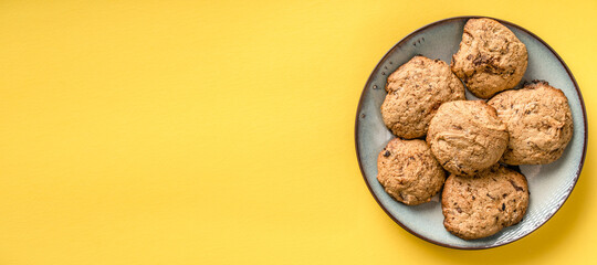 Close up top view on crunchy oatmeal chip cookies fresh baked biscuits with chocolate and cocoa in a plate on the yellow modern abstract background - homemade food concept copy space