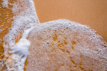 Sea waves and foam in sandy beach in evening.