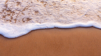 Sea waves and foam in sandy beach in evening.