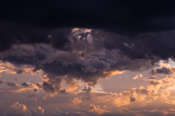 Fototapeta na wymiar Epic sunset storm sky. Big dark black cumulus thunderstorm clouds in yellow orange sunlight background texture