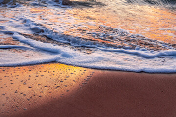 Sea waves and foam in sandy beach in evening.