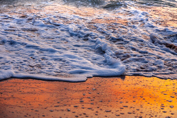 Sea waves and foam in sandy beach in evening.