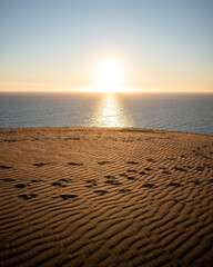 A big dune in front of the sea at sunset, with the sun in the center