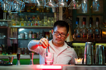 Bartender preparing tasty mixed alcoholic drink with ice cube in decorated cocktail glass on bar counter for customer in nightclub. Celebration party, nightlife business and alcohol addiction concept