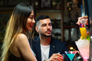 Asian woman talking to boyfriend with drinking alcoholic cocktail at bar counter in nightclub. Male bartender mixologist preparing mixed alcoholic drink with decorate cocktail glass at bar counter