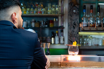 Handsome Caucasian man sitting at bar counter holding whiskey glass with ice cube and drinking alcoholic drink from barman in nightclub. Nightlife holiday party celebration and small business concept