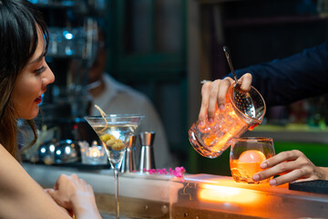 Bartender preparing tasty mixed alcoholic drink with ice cube in decorated cocktail glass on bar counter for customer in nightclub. Celebration party, nightlife business and alcohol addiction concept