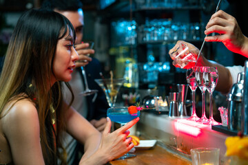 Bartender preparing tasty mixed alcoholic drink with ice cube in decorated cocktail glass on bar counter for customer in nightclub. Celebration party, nightlife business and alcohol addiction concept