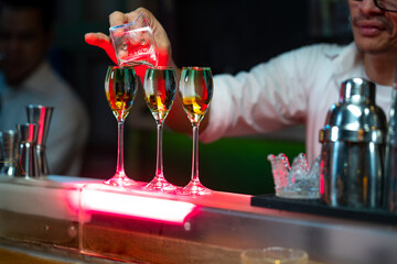 Bartender preparing tasty mixed alcoholic drink with ice cube in decorated cocktail glass on bar counter for customer in nightclub. Celebration party, nightlife business and alcohol addiction concept