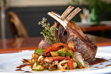 Roasted rack of lamb or rack of veal accompanied with vegetables and sauce, served on white plate...